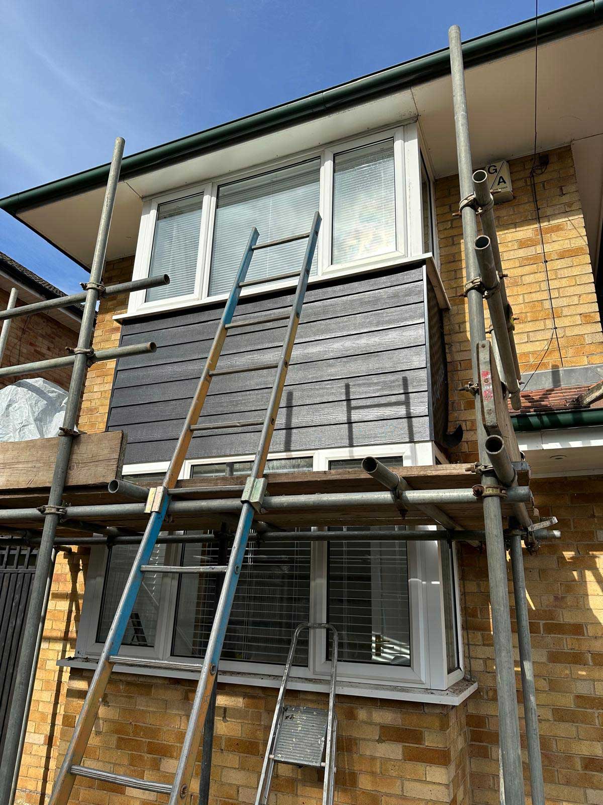 Front elevation of a detached house clad in dark grey weatherboard with white fascias and downlights under the eaves