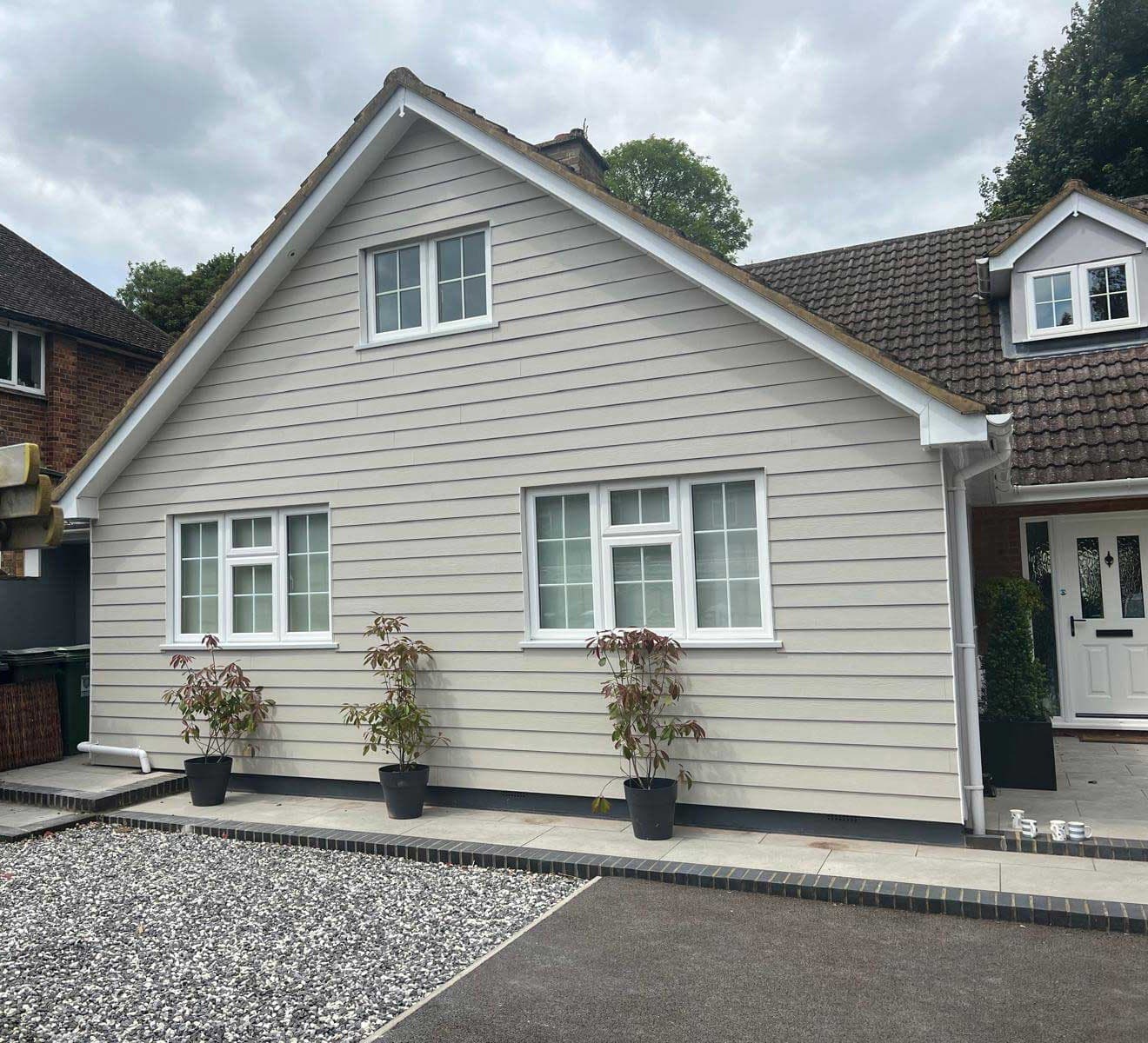 Front elevation of a detached house clad in dark grey weatherboard with white fascias and downlights under the eaves