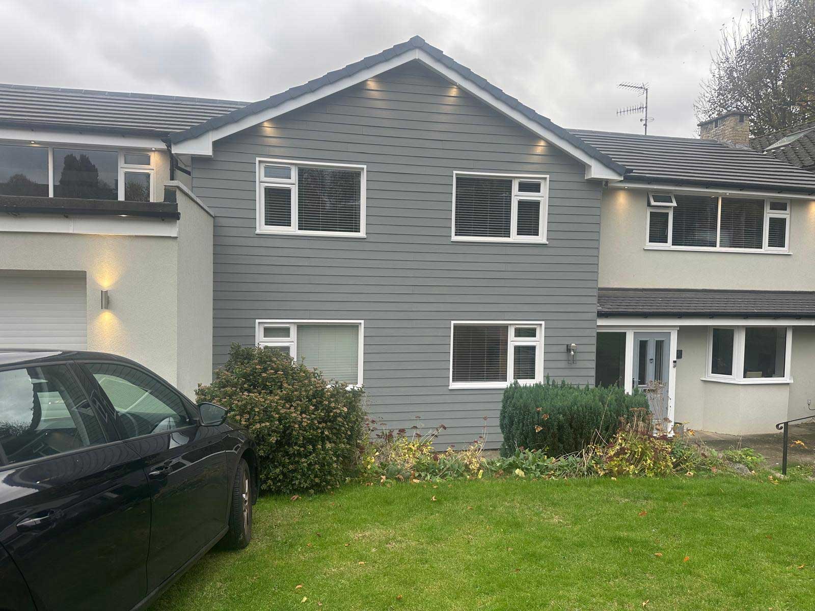 Front elevation of a detached house clad in dark grey weatherboard with white fascias and downlights under the eaves
