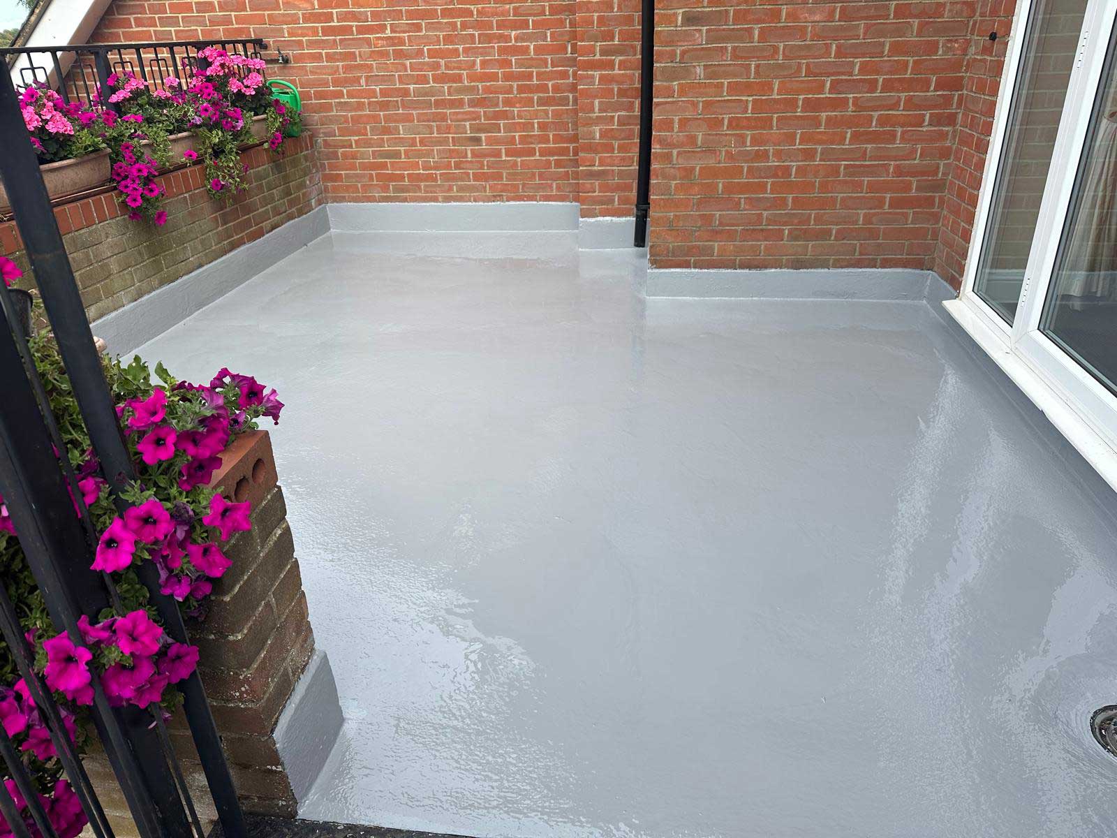 Finished grey GRP fibreglass balcony roof with continuous upstands, flower boxes on the railing behind