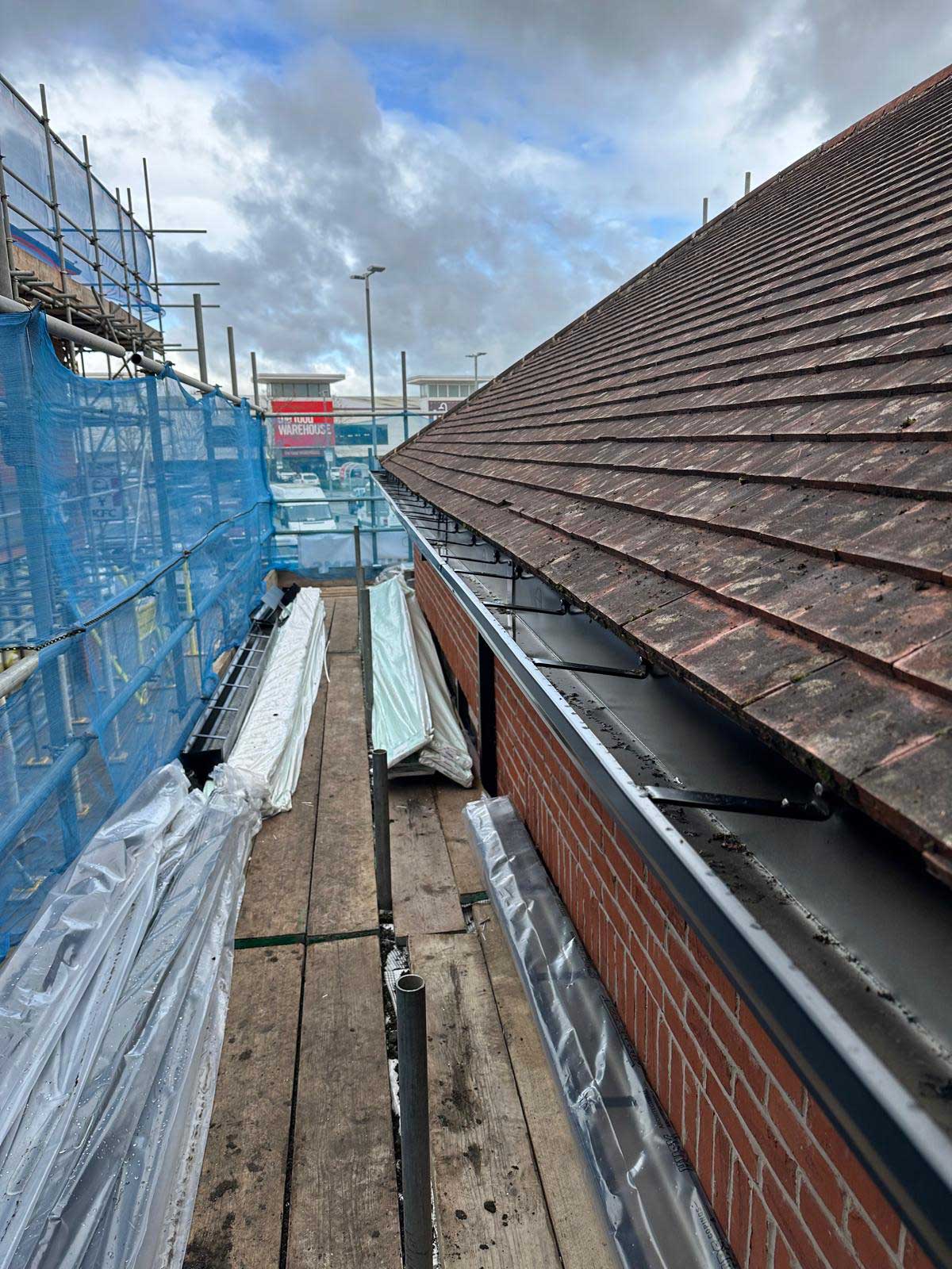 New black guttering and fascia fitted along the eaves of a plain clay tiled roof, viewed from the scaffold