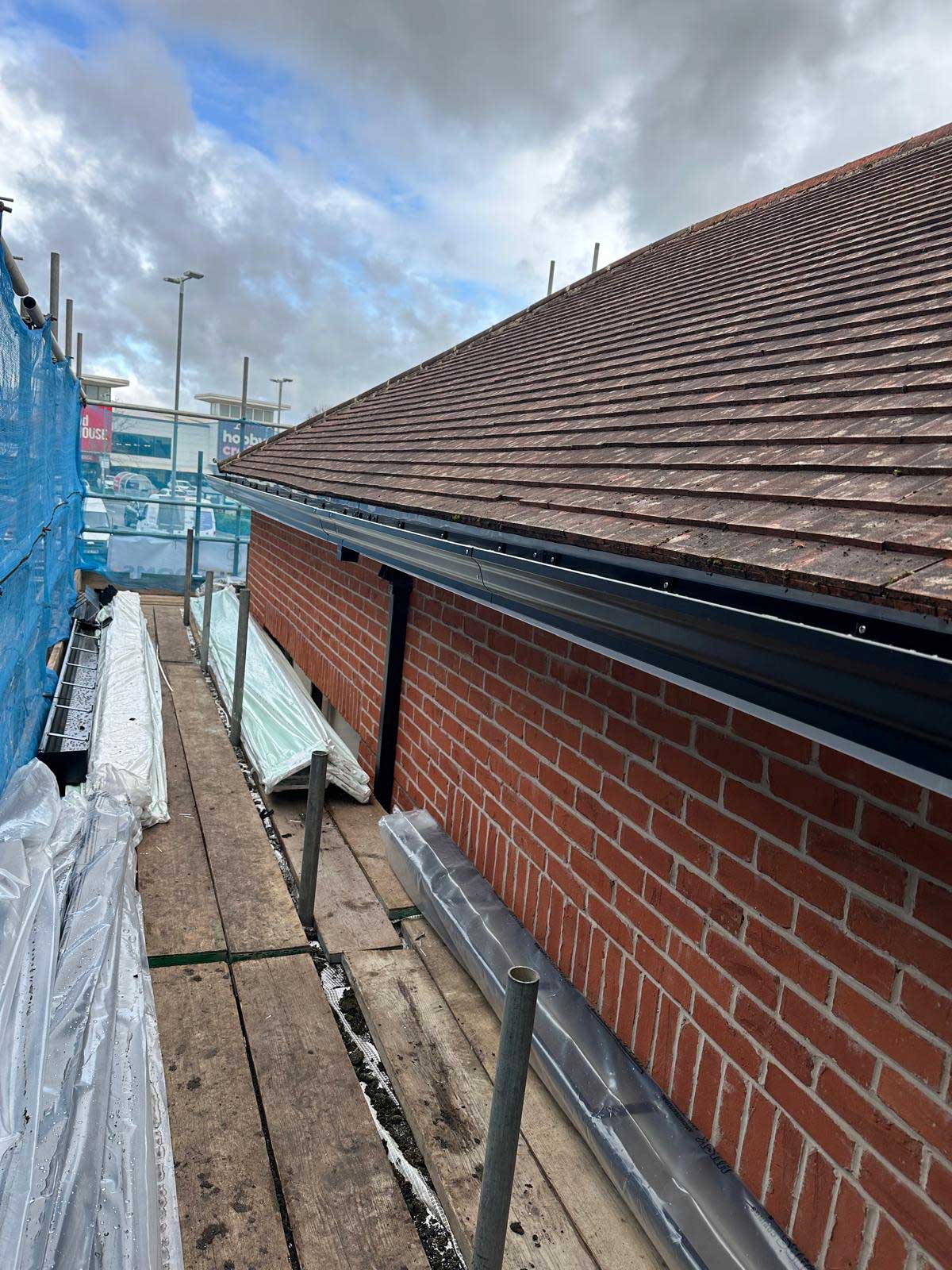 New black guttering and fascia fitted along the eaves of a plain clay tiled roof, viewed from the scaffold