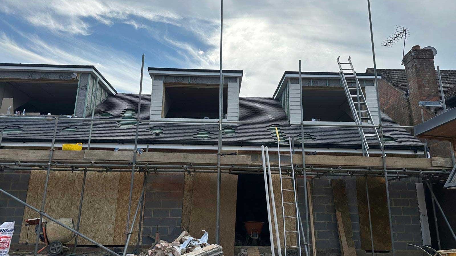Three new dormers framed into a tiled roof during a loft conversion, with the roof stripped back around them