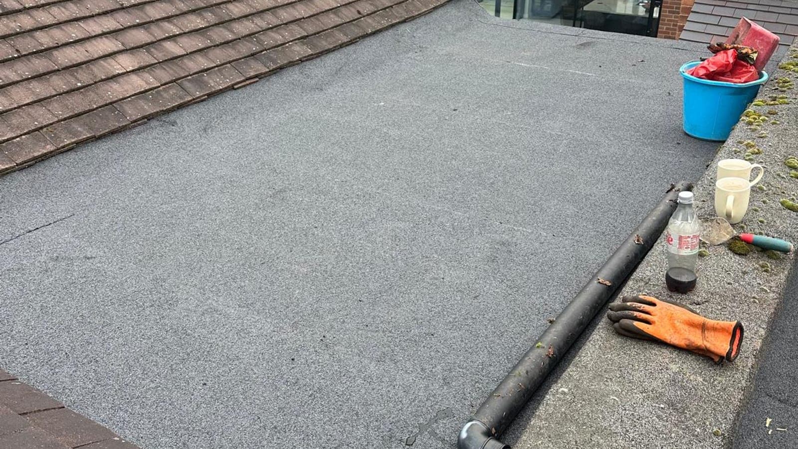 Newly laid felt flat roof between two tiled pitched roofs, with a new downpipe run along the parapet
