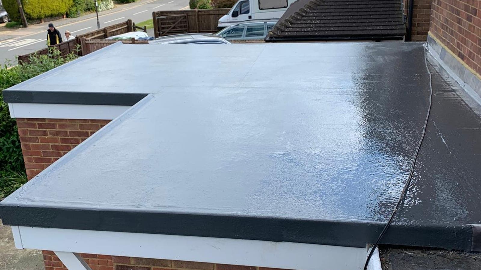 Finished grey GRP fibreglass garage roof with black drip trims, on a brick garage beside the house