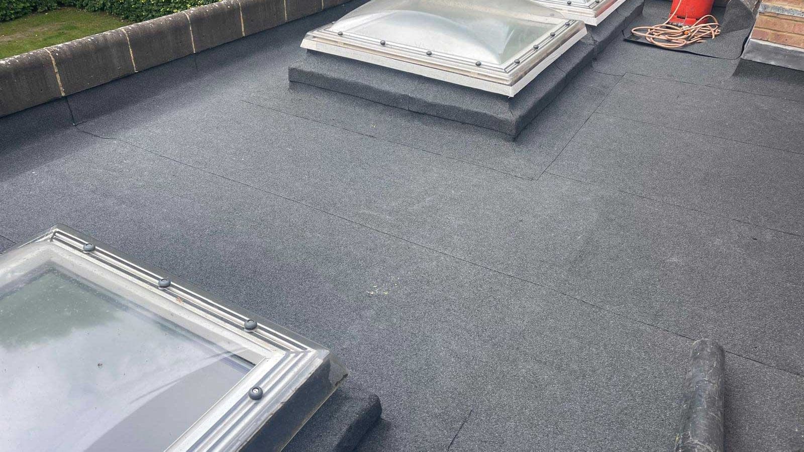 Torch-on felt flat roof with two domed rooflights set on felt upstands, bounded by a coped parapet wall