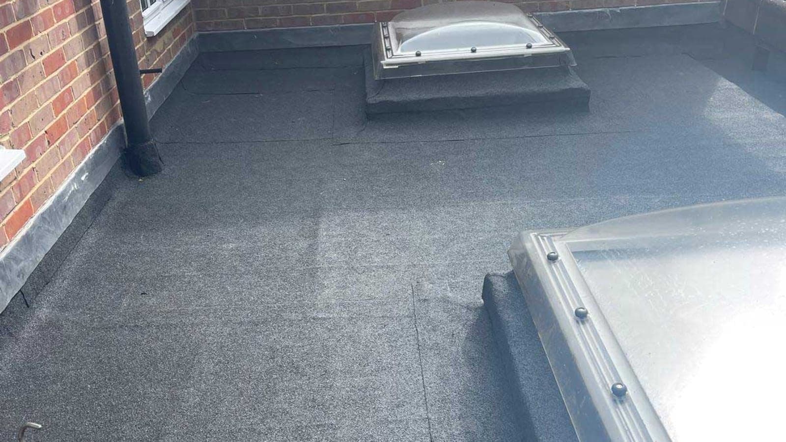 Newly laid torch-on felt flat roof with two rooflights, enclosed by brick walls with a cast downpipe