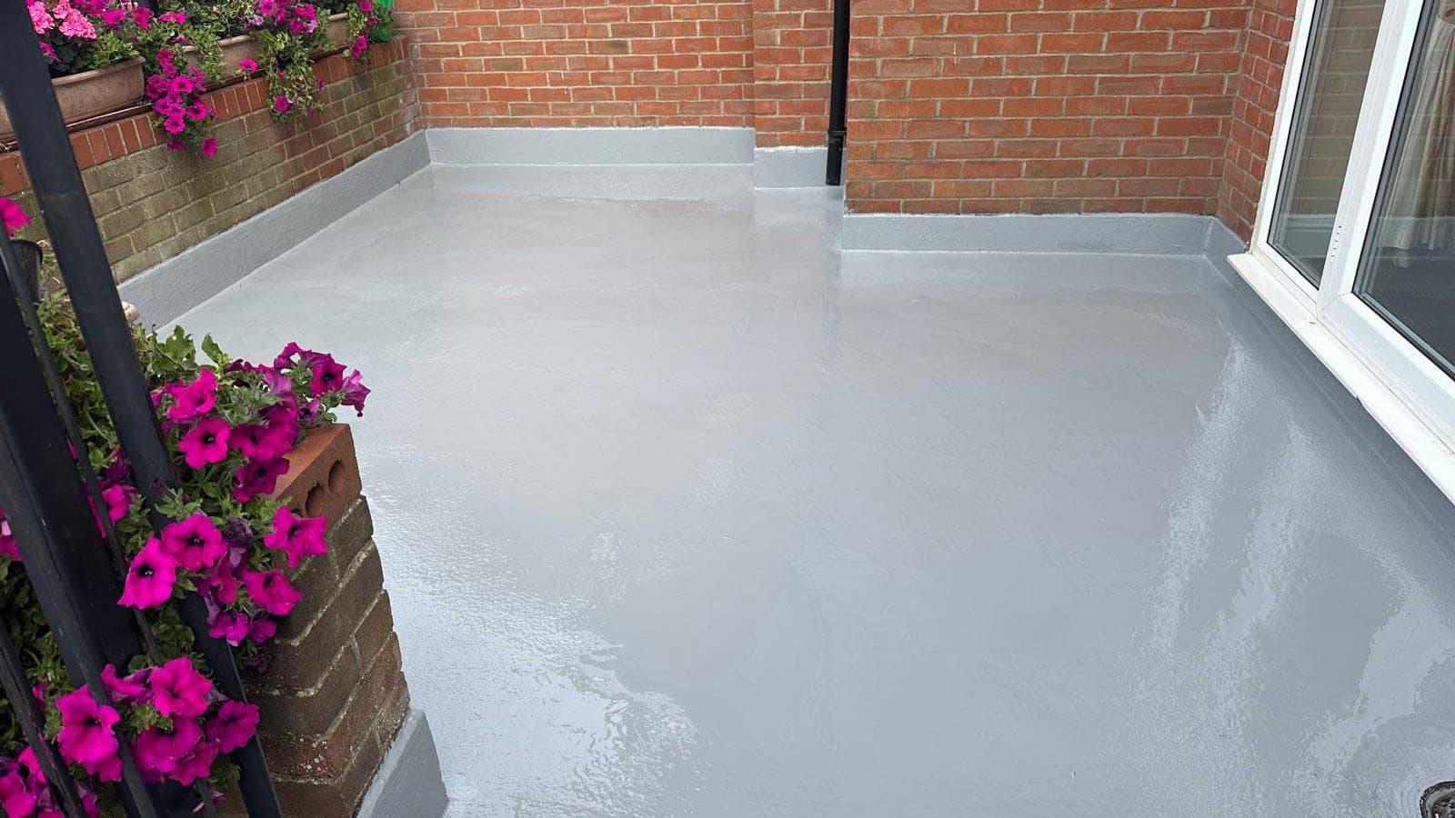 Finished grey GRP fibreglass balcony roof with continuous upstands, flower boxes on the railing behind