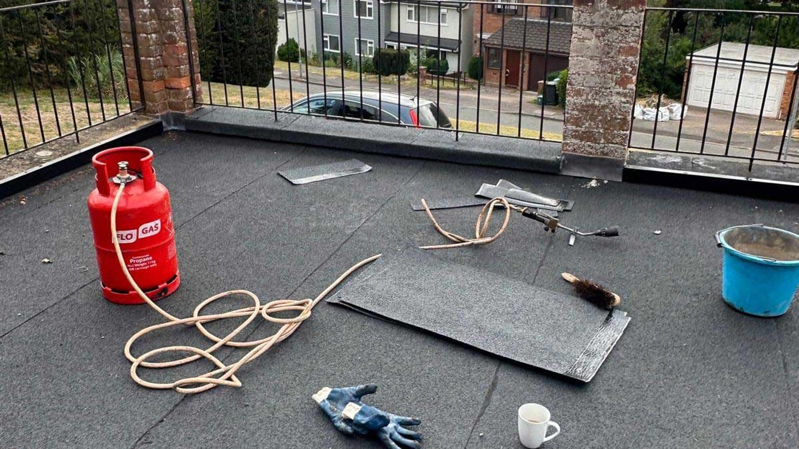 Torch-on felt being laid on a balcony roof, with the gas torch, propane bottle and trowel set out on the finished section