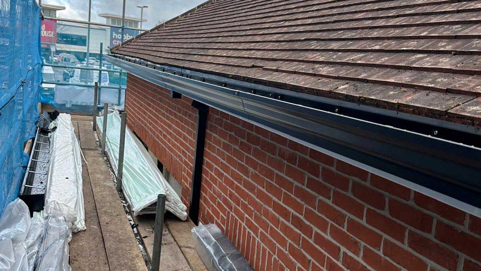 New black guttering and fascia fitted along the eaves of a plain clay tiled roof, viewed from the scaffold