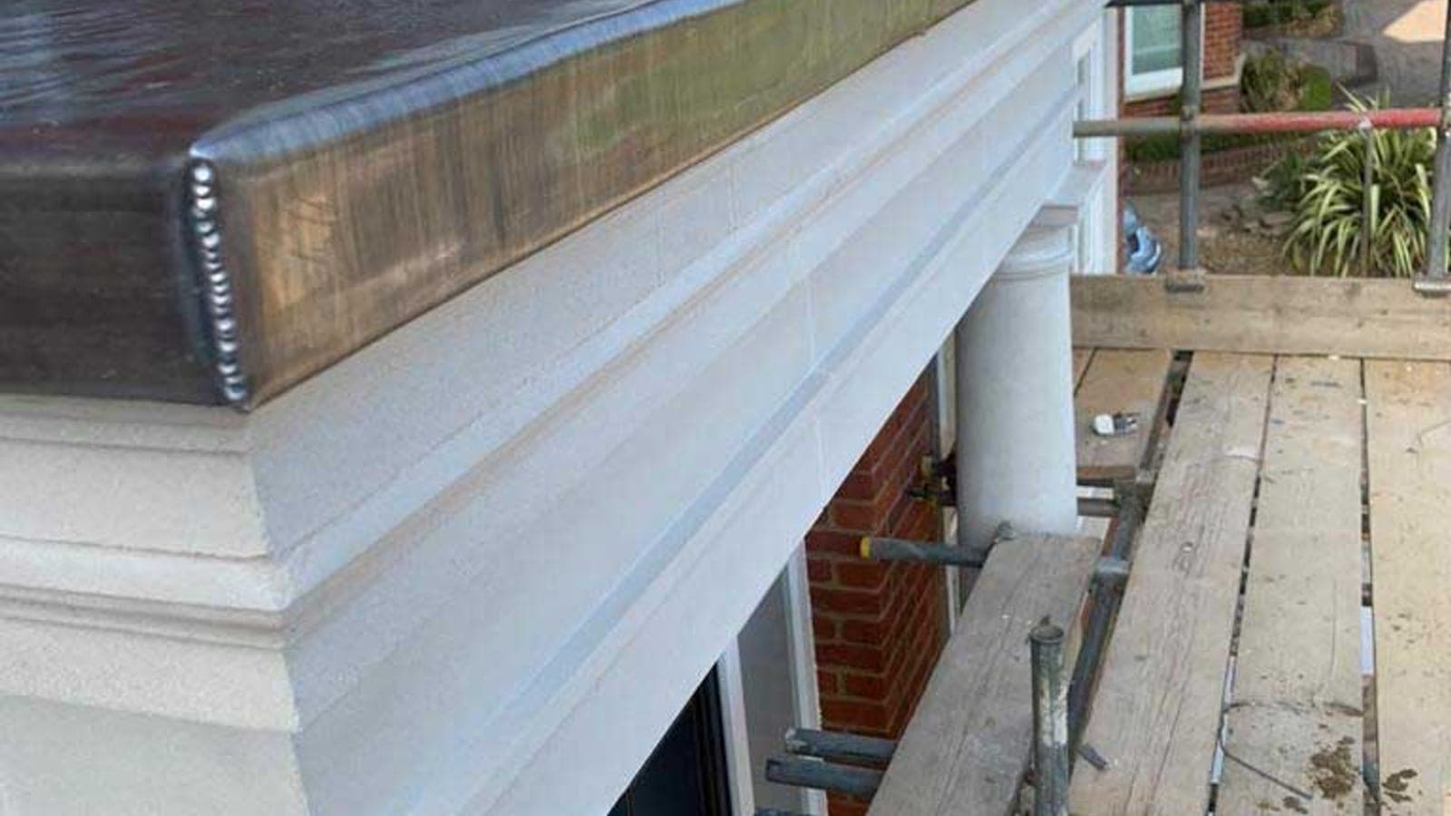 Lead-covered bay roof with welded rolls running down to a drip, above a painted stone cornice