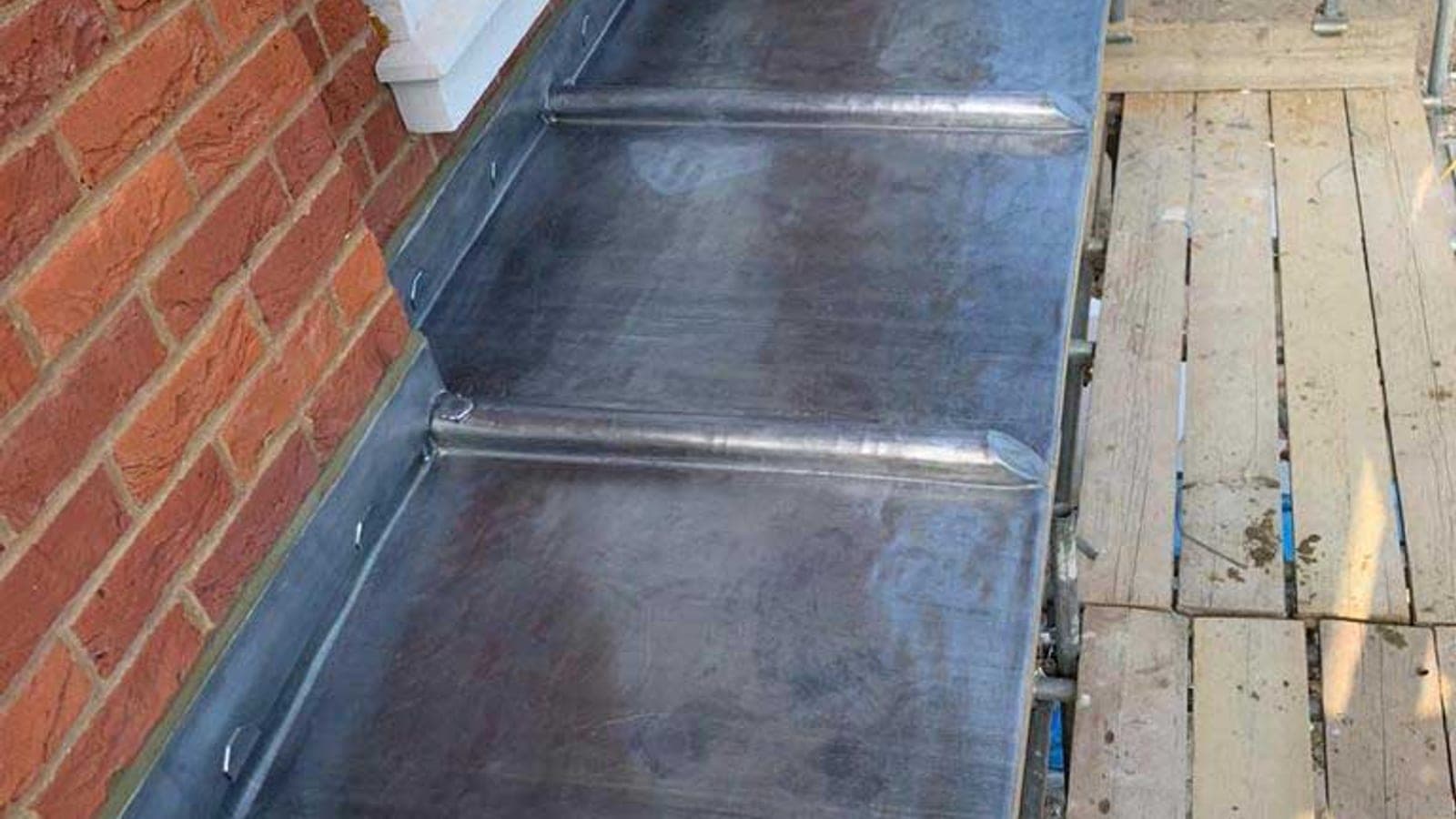 Overhead view of a finished lead bay roof showing four evenly spaced welded rolls and a clean drip edge