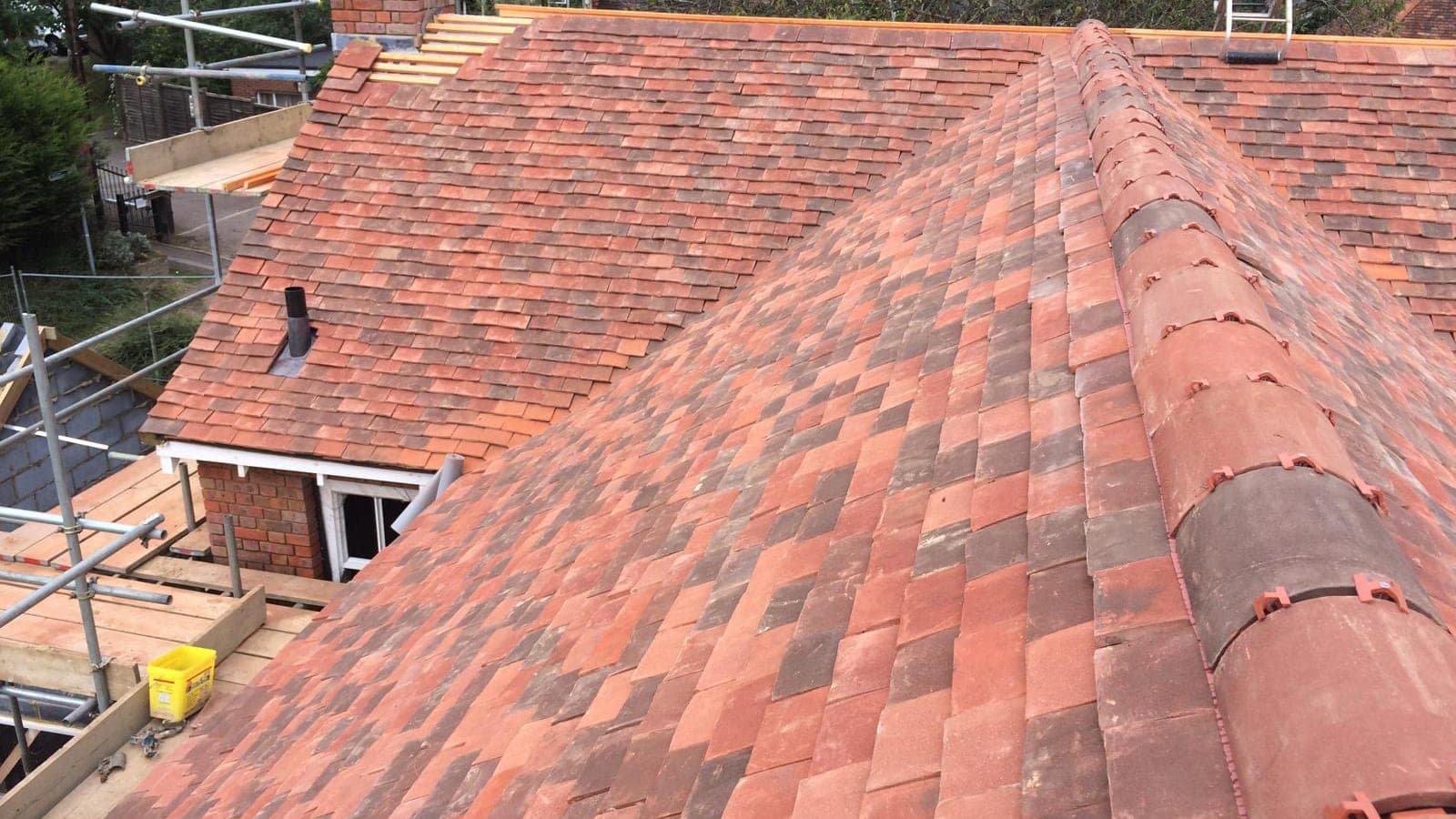 Finished clay plain tile roof in blended reds with a clay half-round ridge and a small tiled dormer below