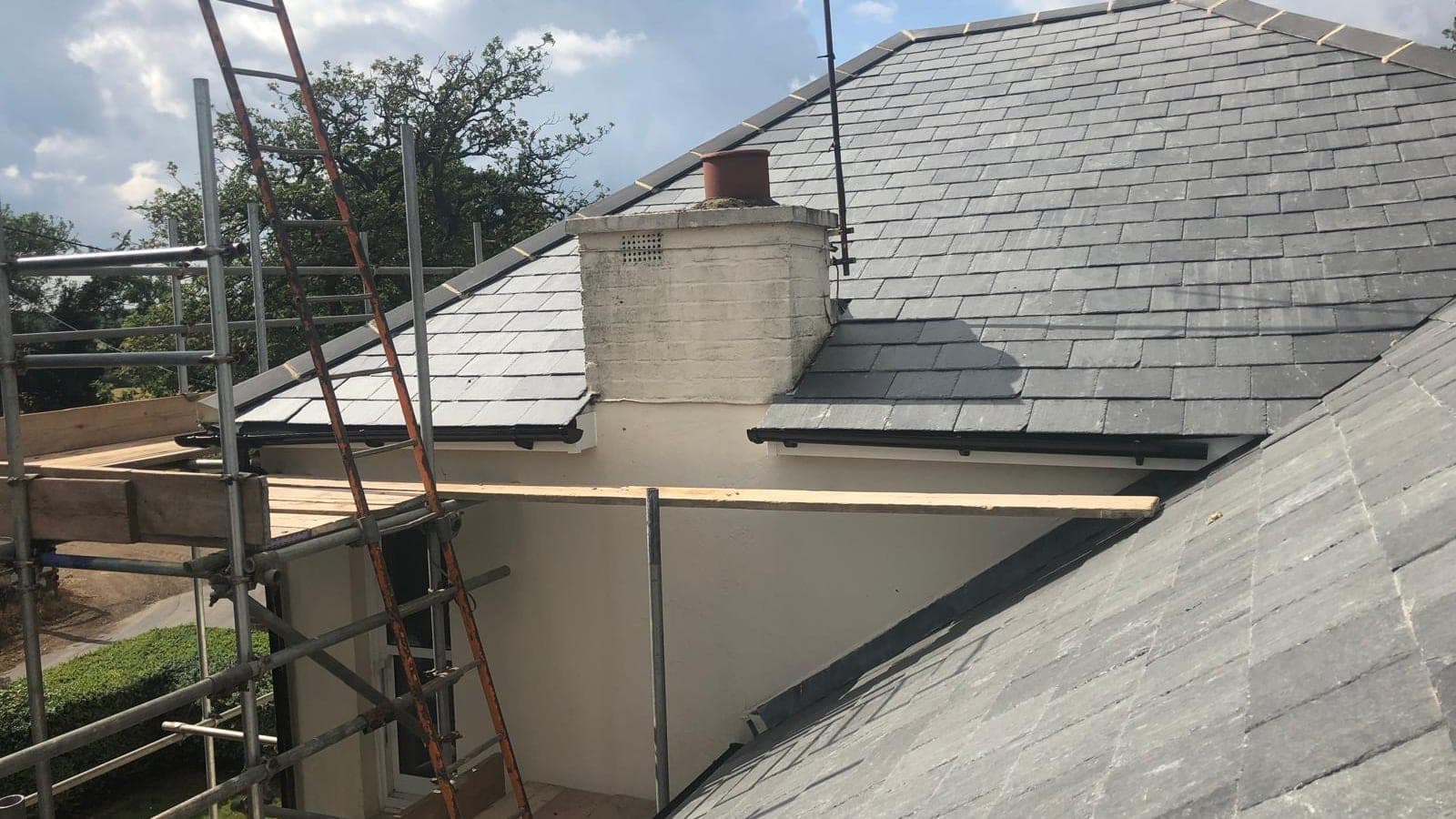 New blue-grey slate roof with a rendered chimney stack and lead soakers, seen from the scaffold