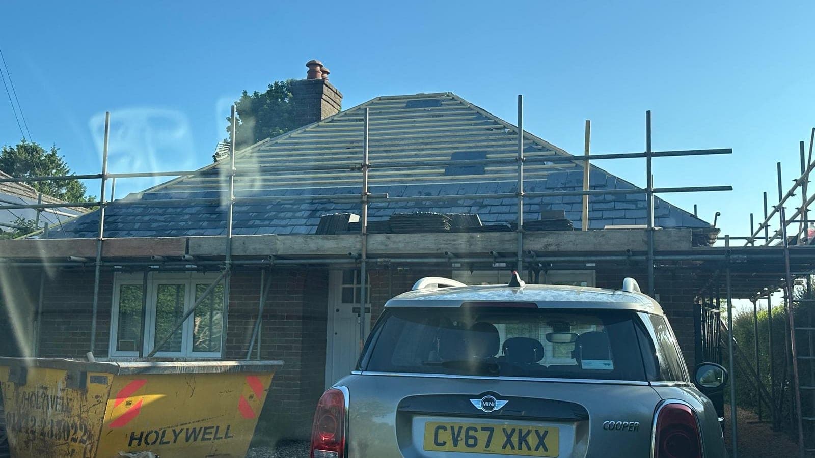 Bungalow roof stripped back to the battens with new slate being laid up the hip, scaffold and skip in the drive