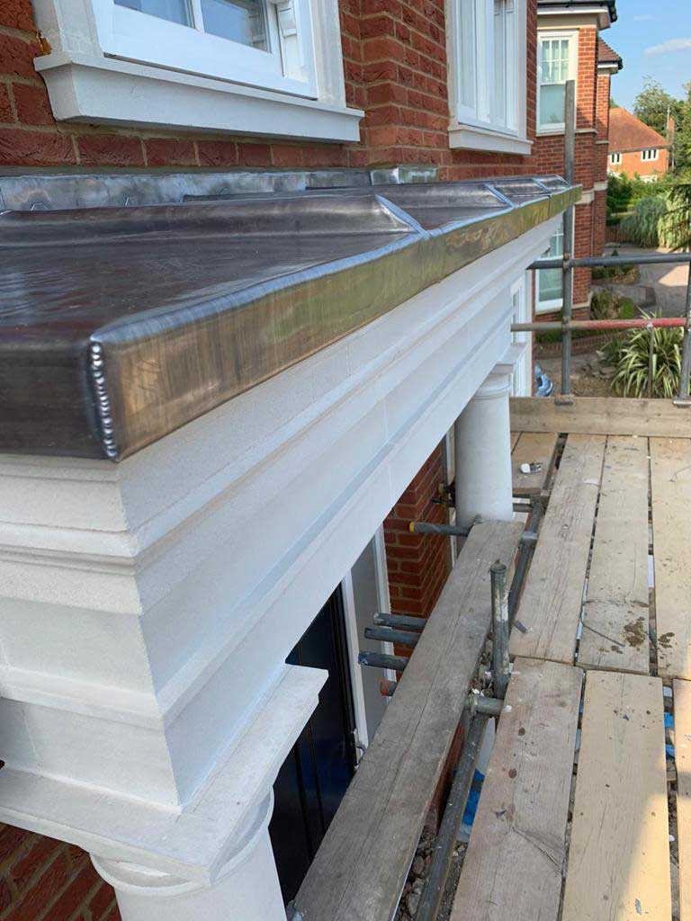 Lead-covered bay roof with welded rolls running down to a drip, above a painted stone cornice