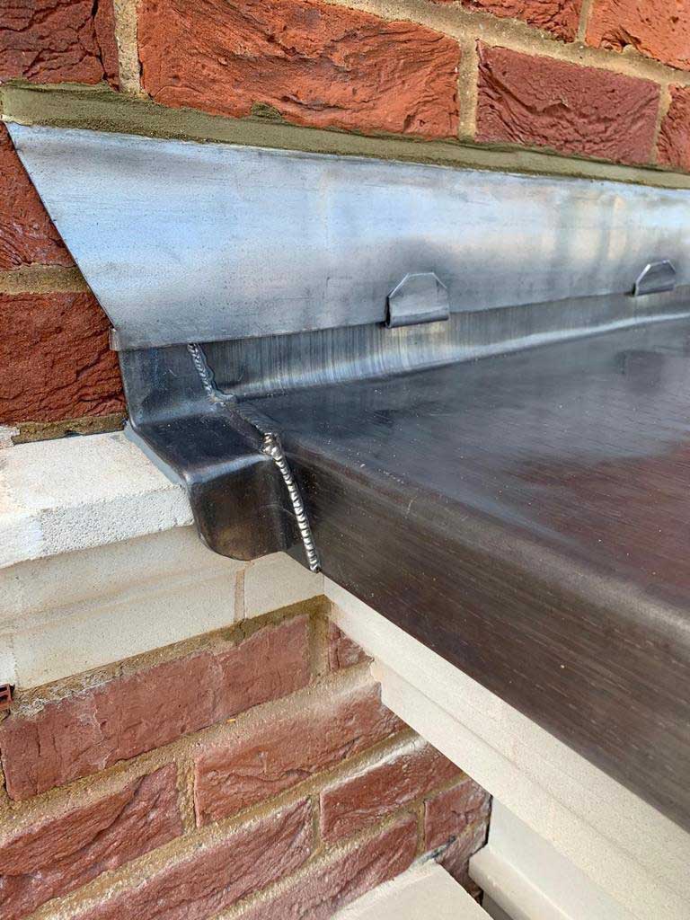 Lead-covered bay roof with welded rolls running down to a drip, above a painted stone cornice