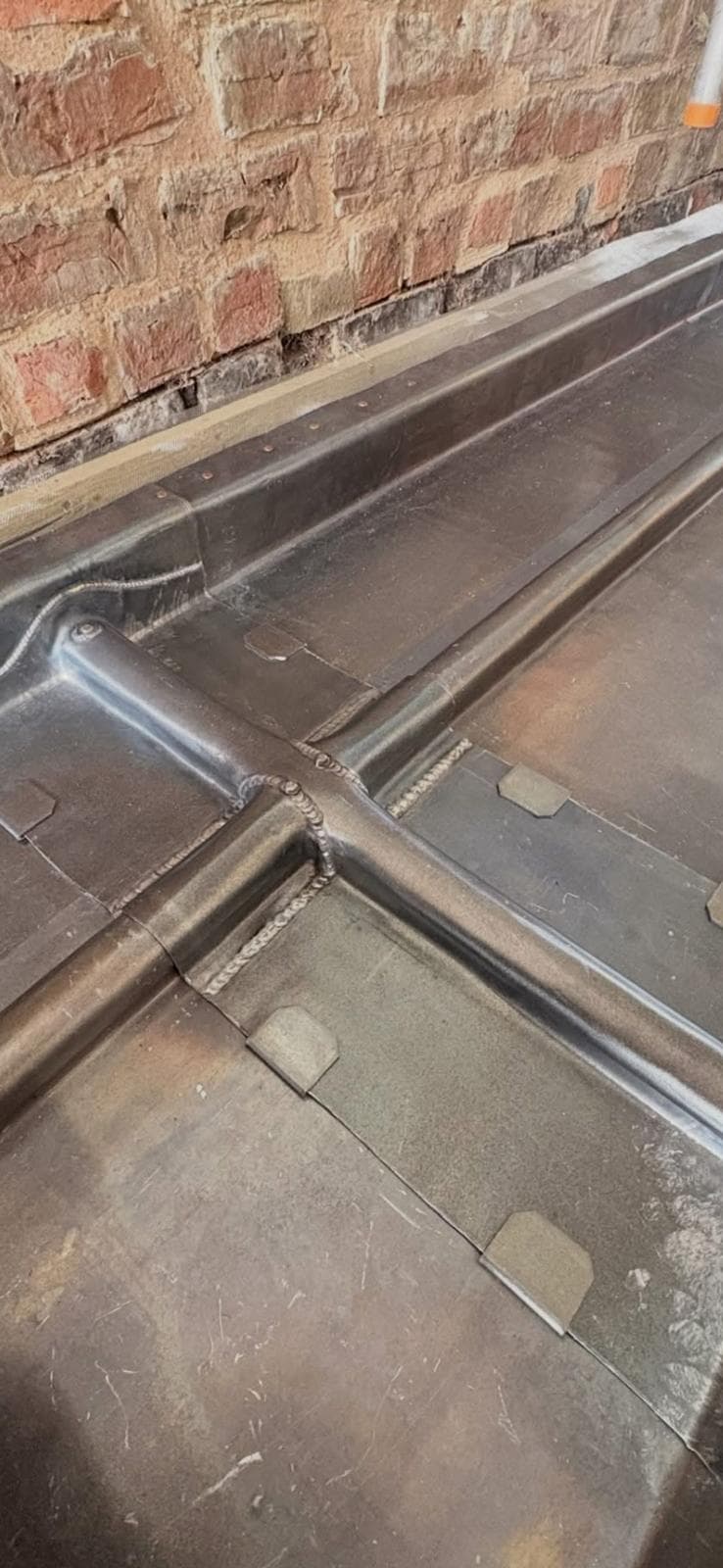 Lead-covered bay roof with welded rolls running down to a drip, above a painted stone cornice