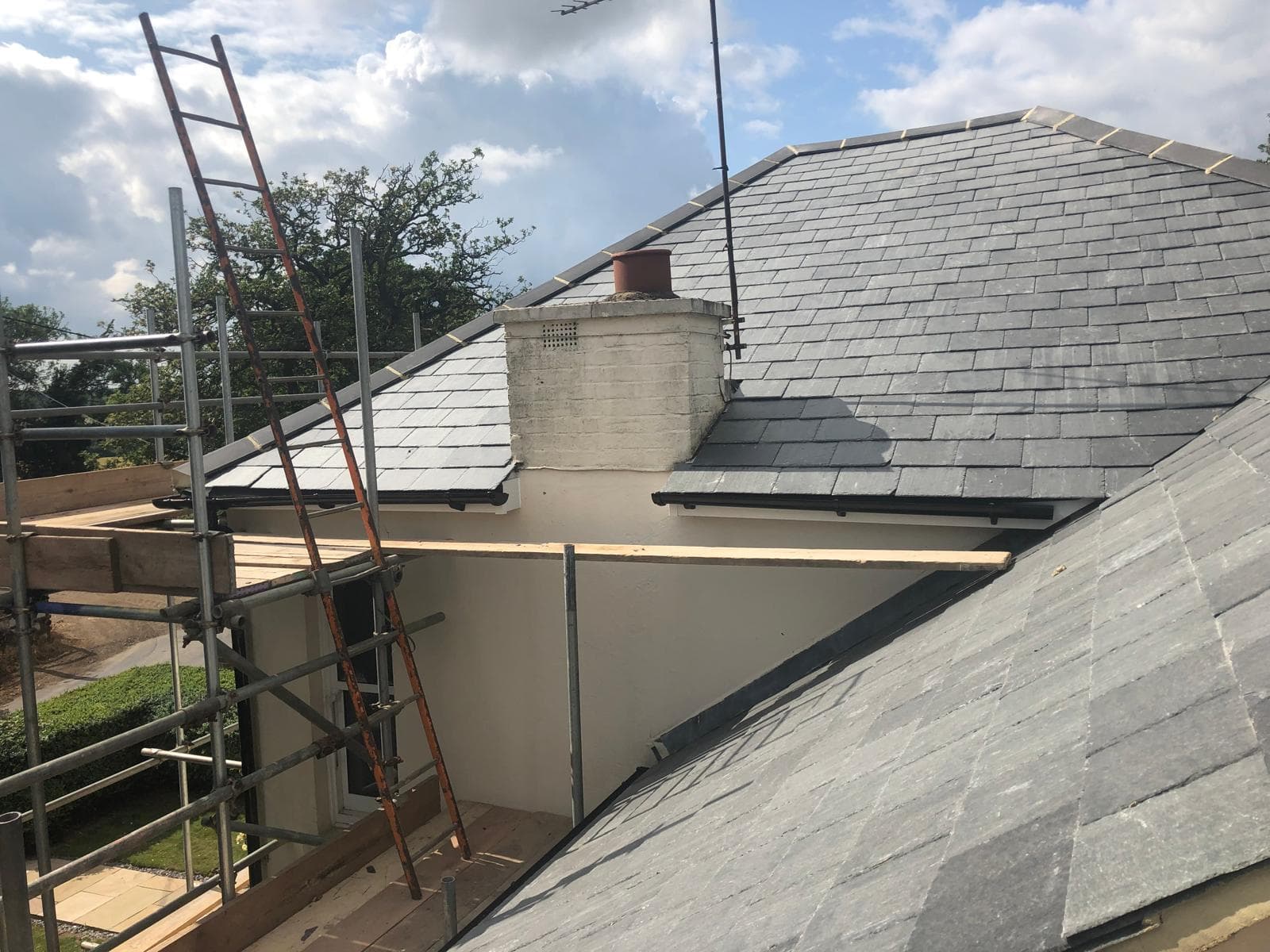 Newly laid blue-grey slate roof with a flush rooflight and a clean hip, seen from the scaffold