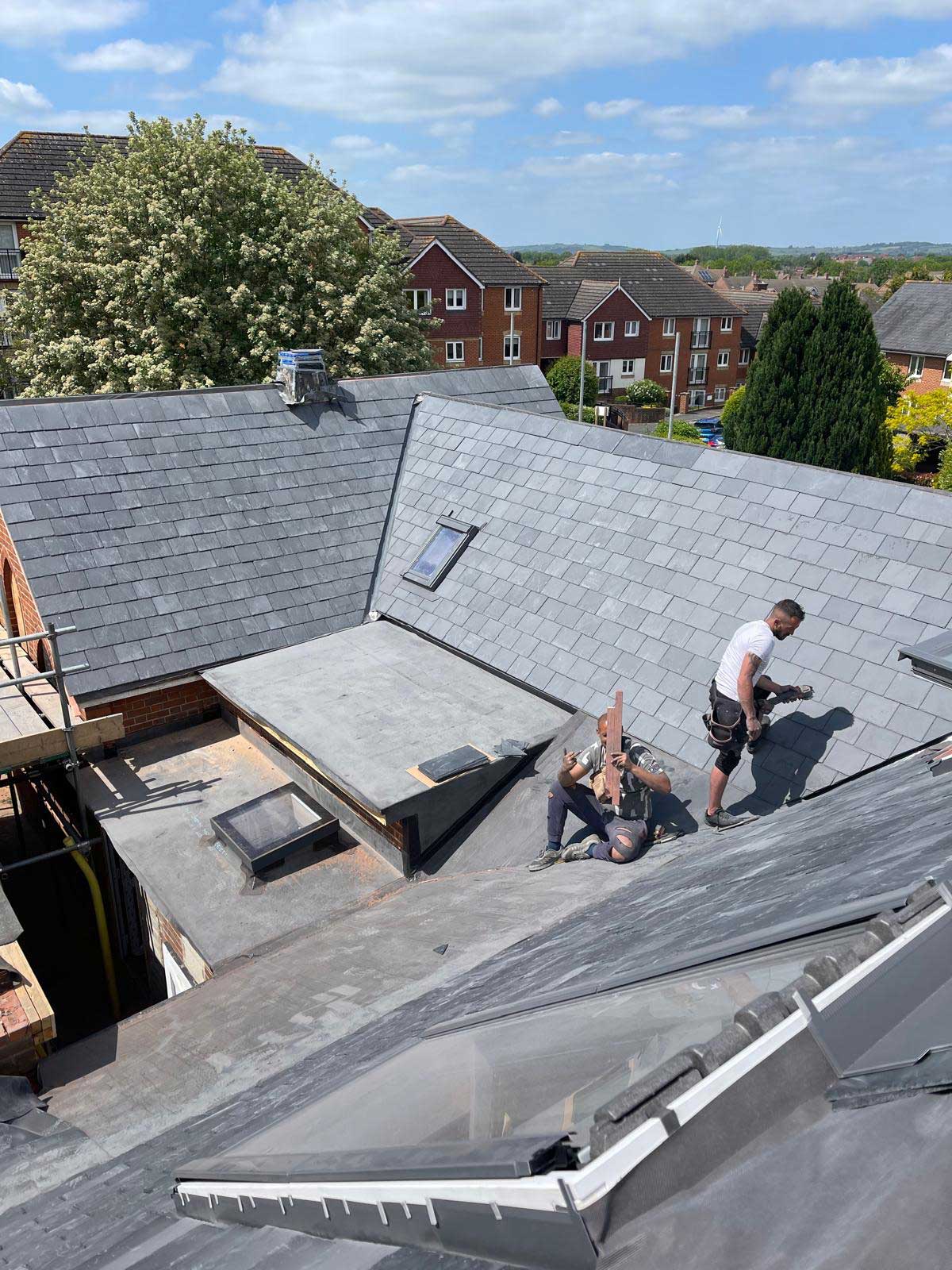 Newly laid blue-grey slate roof with a flush rooflight and a clean hip, seen from the scaffold