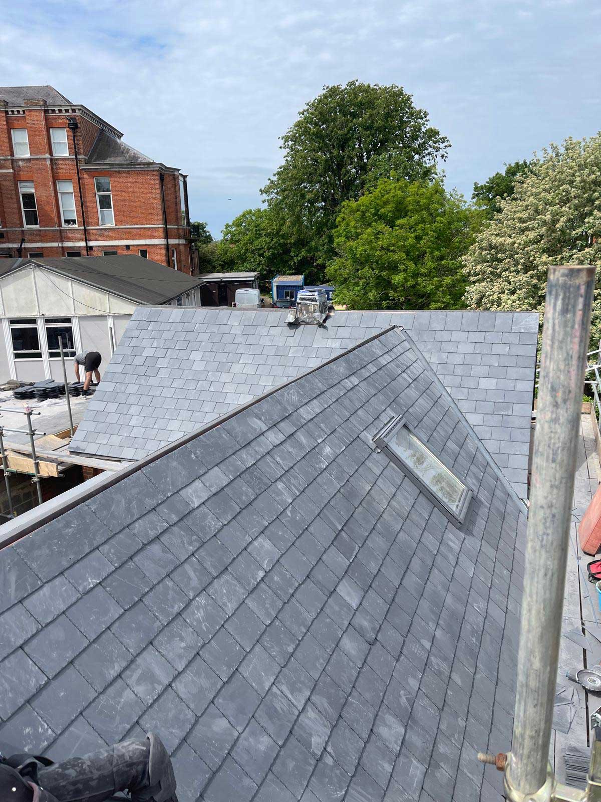 Newly laid blue-grey slate roof with a flush rooflight and a clean hip, seen from the scaffold
