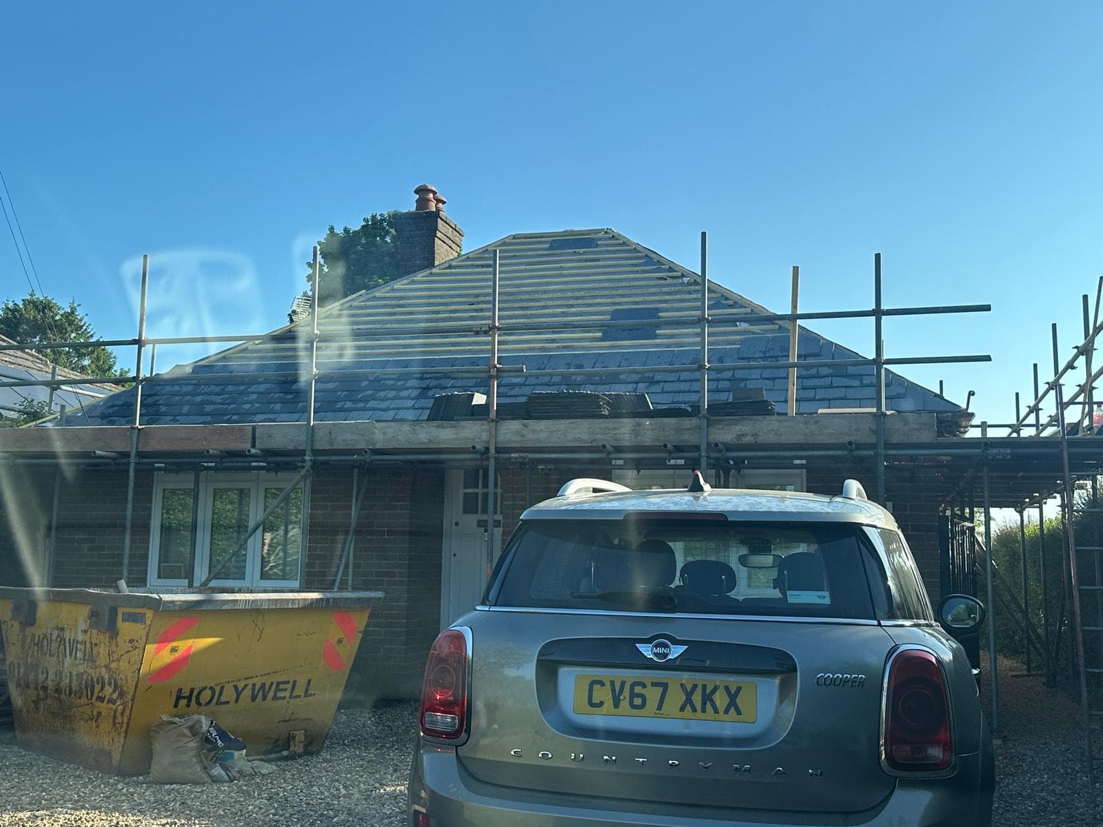 Newly laid blue-grey slate roof with a flush rooflight and a clean hip, seen from the scaffold